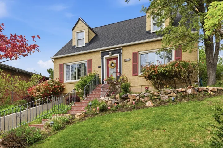Charming stucco exterior residence featuring a dark shingle roof and prominent dormer windows
