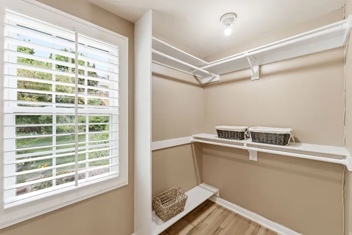 Walk-in closet featuring plantation shutters, wood-finish flooring, and multiple shelving and hanging rods