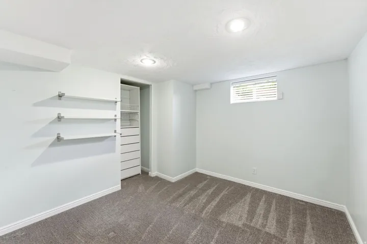 Carpeted interior space featuring recessed lighting, a window with blinds, and built-in shelving