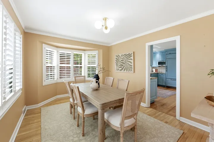 Dining area featuring a bay window with plantation shutters, hardwood flooring, and crown molding