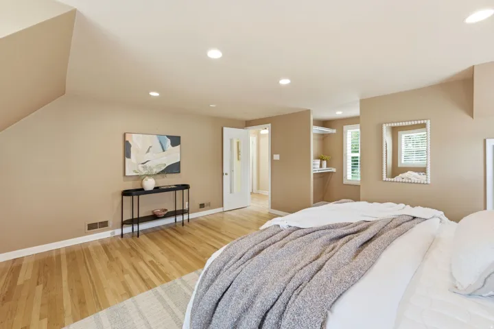 Hardwood flooring throughout the room, featuring recessed ceiling lighting, a white paneled door, and a dedicated storage nook with shelving