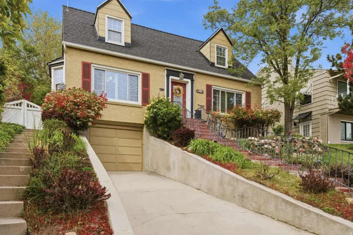 Traditional-style residence featuring a dormered roofline, shuttered windows, a built-in garage with a single door, a concrete driveway, and tiered landscaping