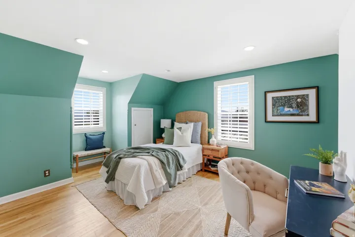 Recessed lighting illuminates this room featuring sloped ceilings, two windows with white plantation shutters, and wood-finish flooring