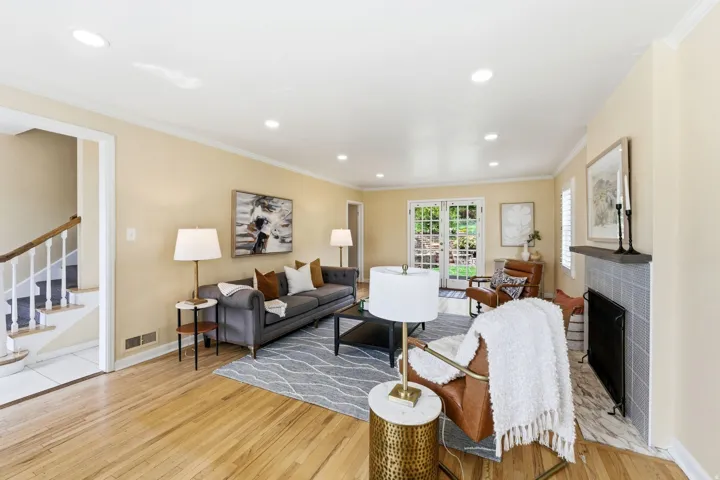 Spacious living area featuring light wood flooring, recessed lighting, a fireplace with a tiled surround, white French doors, and a staircase with white balusters
