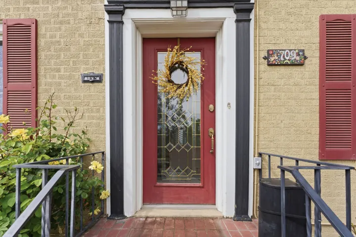 Red entry door with an ornate glass insert, flanked by black decorative pillars and white trim