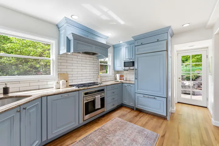 Kitchen featuring light blue cabinetry, stainless steel appliances, light-toned countertops, white subway tile backsplash, and wood-finish flooring
