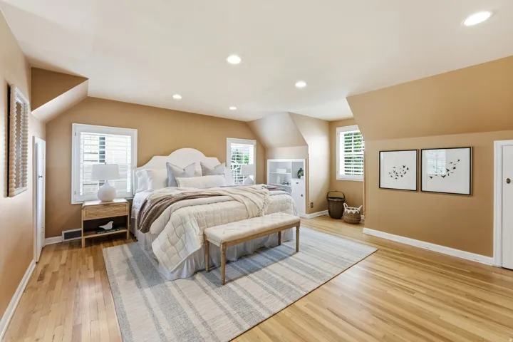 Spacious room with pitched ceilings, wood-finish flooring, recessed lighting, white louvered window treatments, and a built-in white cabinet with shelving