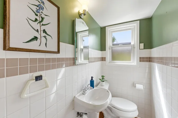 Bathroom with pedestal sink, toilet, and a window providing natural light