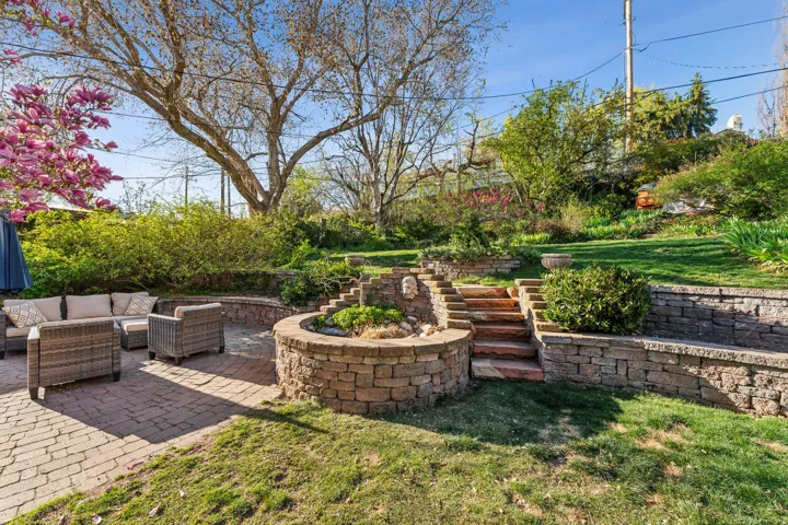 Terraced backyard featuring stone retaining walls, a multi-level water feature, natural stone steps, and a brick paver patio