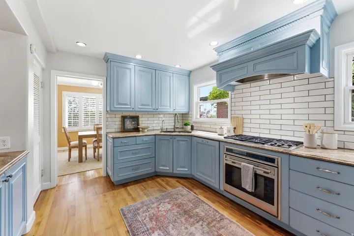 Gourmet kitchen featuring light blue cabinetry, granite countertops, stainless steel appliances, a tile backsplash, and wood-finish flooring