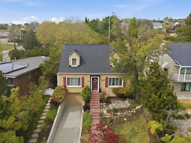 Traditional style residence featuring a dark shingle roof, dormer windows, and yellow siding with red shutters