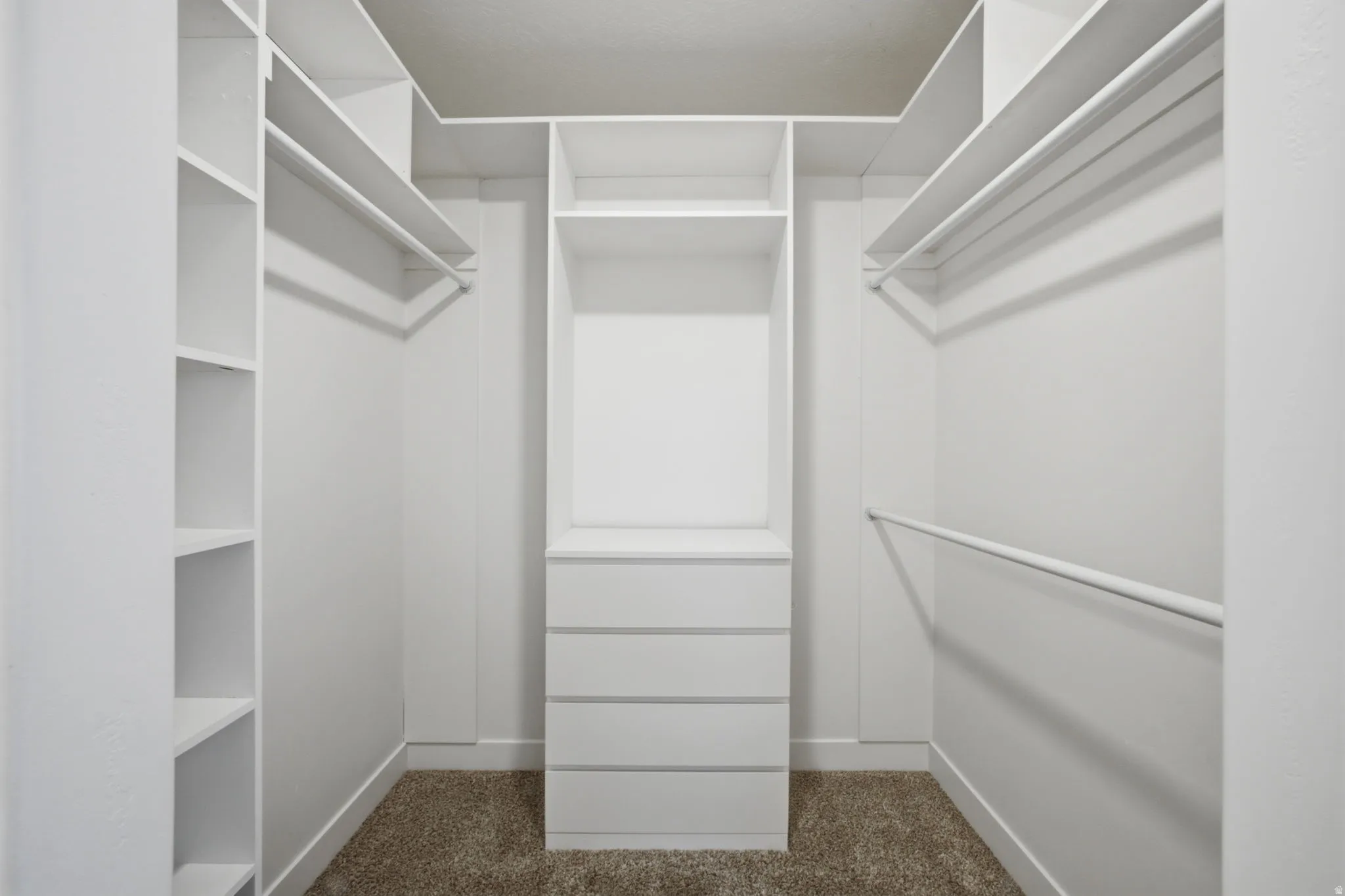 Walk-in closet featuring white built-in shelving, multiple hanging rods, and a central five-drawer dresser unit