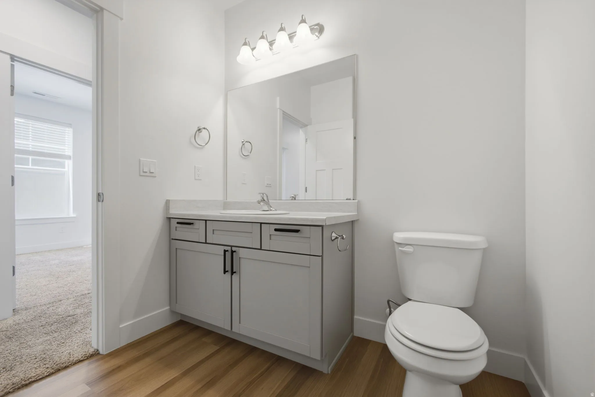 Bathroom featuring a white toilet, light gray vanity with a single basin sink, and a large mirror with a four-bulb light fixture