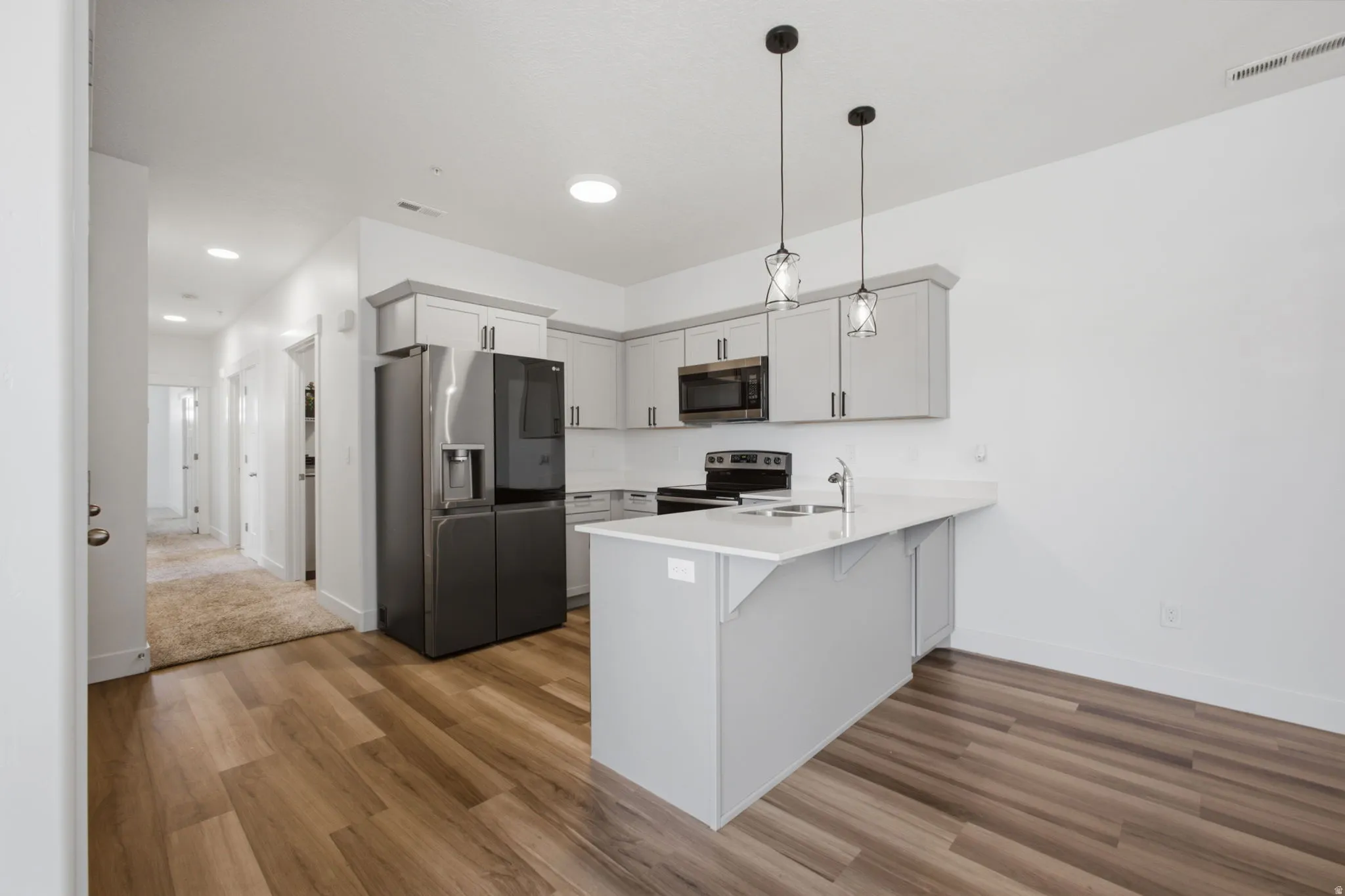 Contemporary kitchen featuring light gray cabinetry, stainless steel appliances, and a central island with a sink