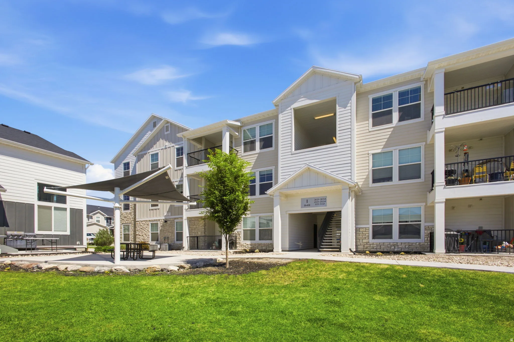 Multi-story residential building featuring light-colored siding, stone accents, and private balconies