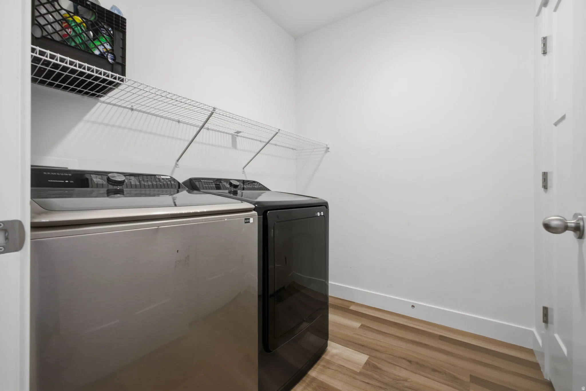 Dedicated laundry area featuring wood-finish flooring, white walls, and built-in wire shelving