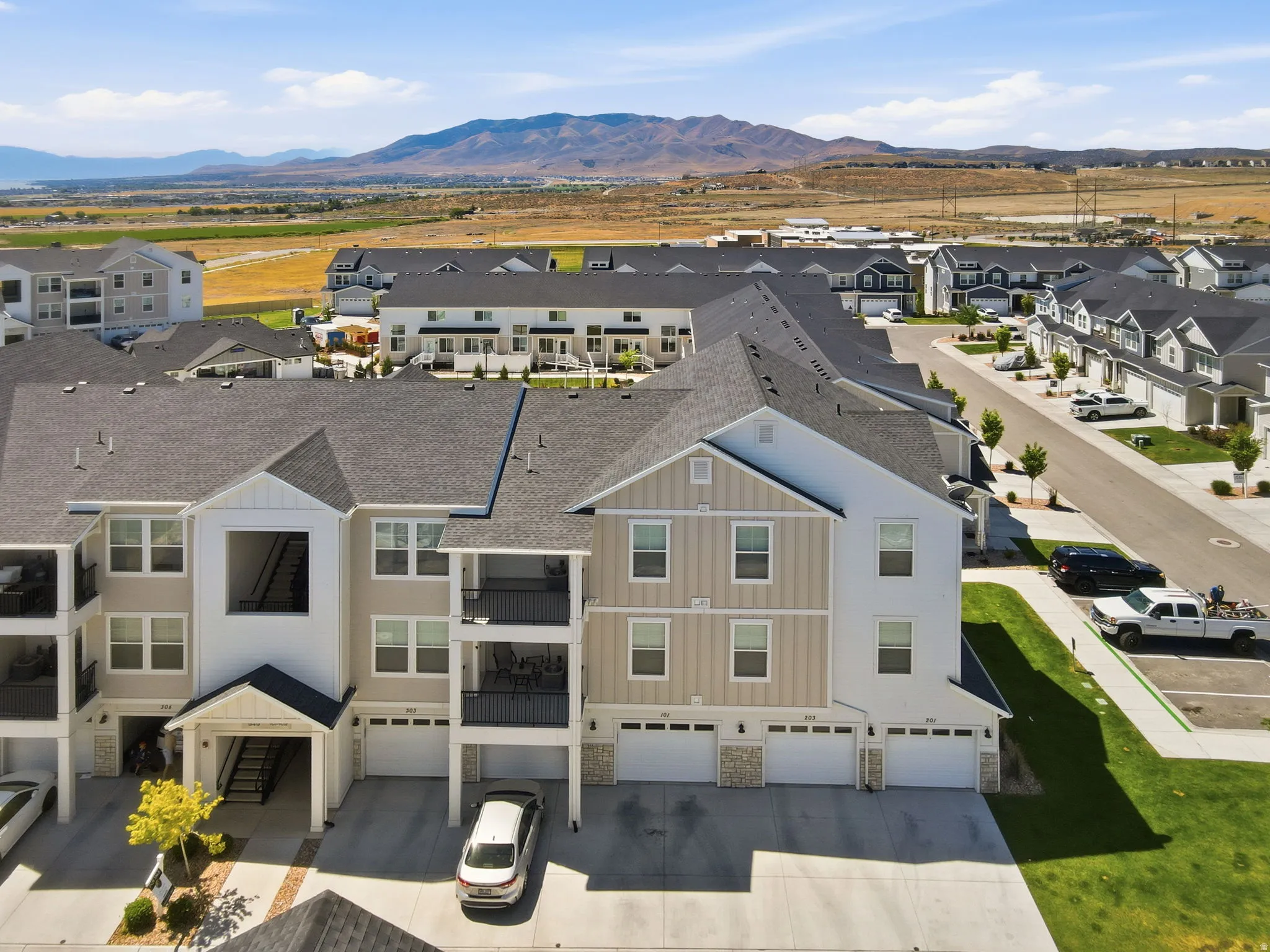 Multi-level residential building featuring private balconies with black railings, individual garages, and a light-toned exterior with stone accents