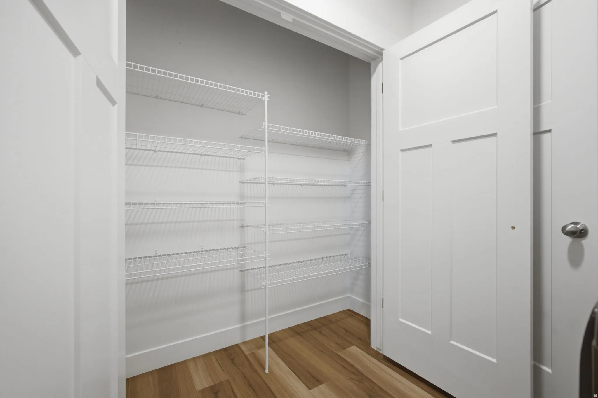 Pantry space featuring wire shelving systems, wood-finish flooring, and crisp white trim