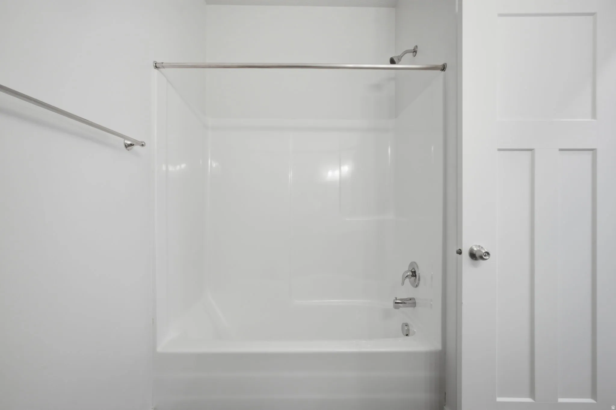 White tub and shower combination with chrome fixtures, a shower rod, and a towel bar