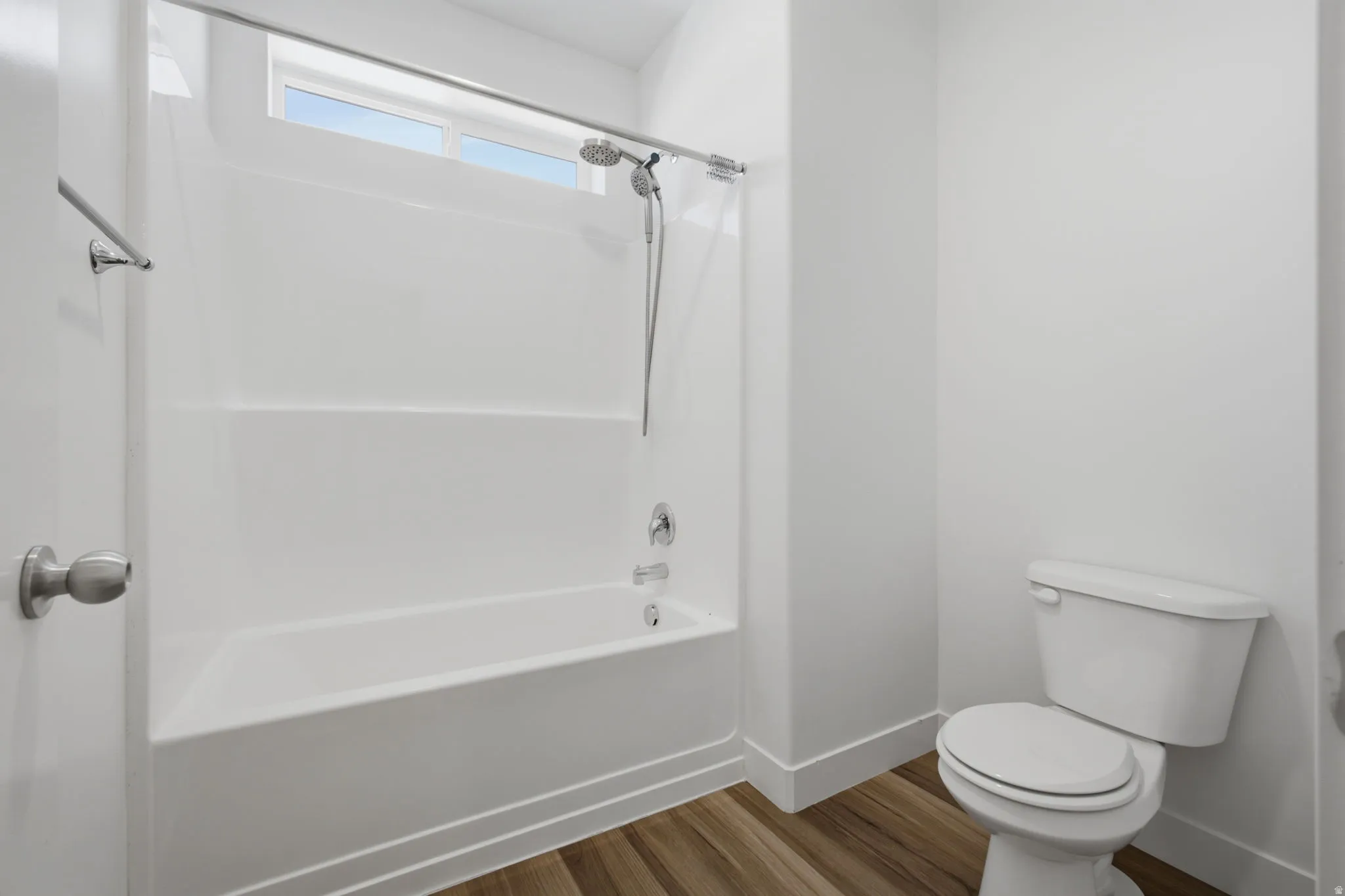 Bathroom with white tub/shower combination, polished chrome fixtures, and a high window offering natural illumination