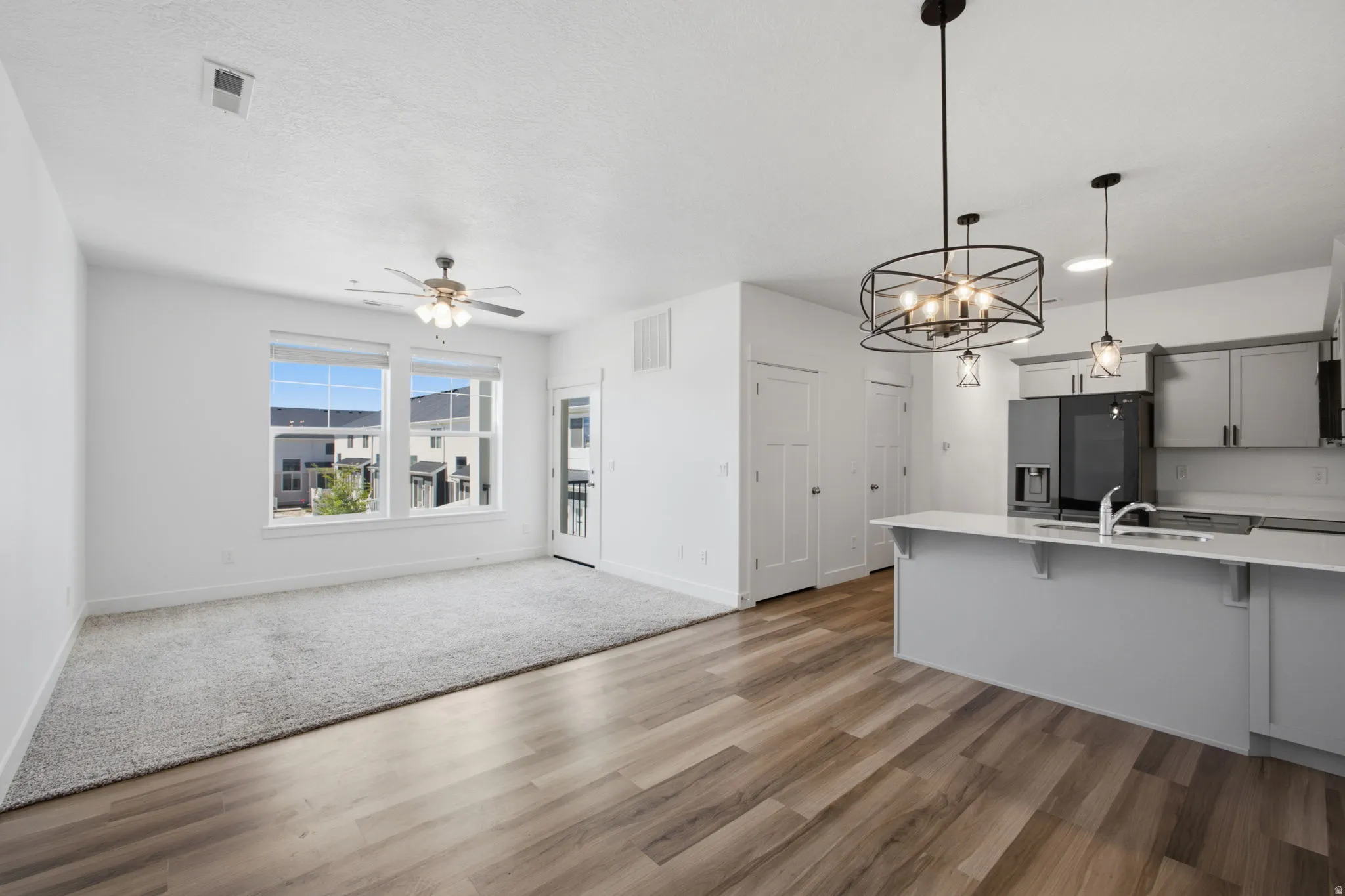 Open-concept living space featuring wood-finish flooring, a contemporary kitchen island with a light-toned countertop, modern pendant lighting, and a ceiling fan