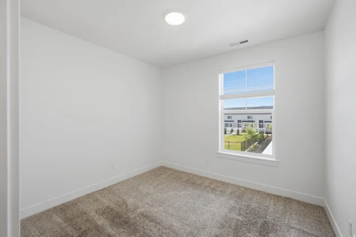 Bright interior room featuring neutral carpeting, white walls, a single window with blinds, and a flush-mount ceiling light fixture