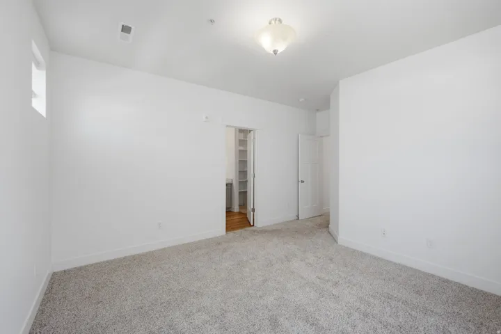 Spacious room with light gray carpeting, neutral wall finishes, a built-in ceiling light fixture, a window with natural light, and a closet with wood-finish flooring and built-in shelving