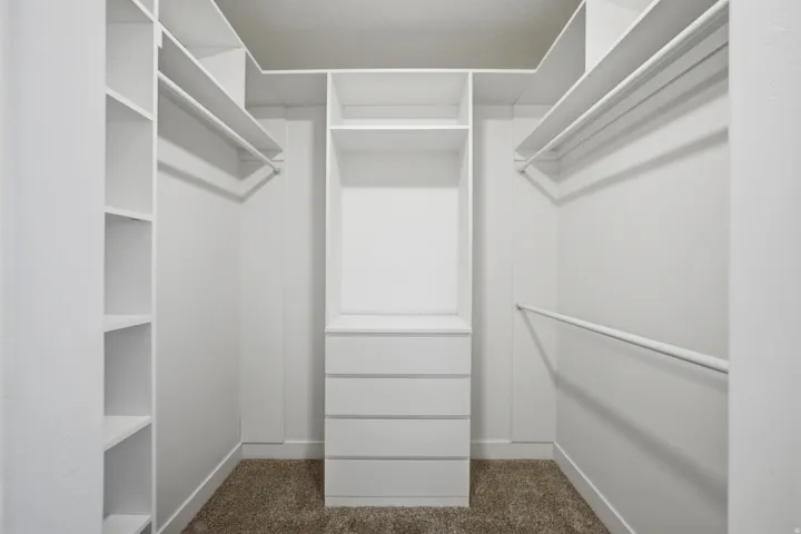 Walk-in closet featuring white built-in shelving, multiple hanging rods, and a central five-drawer dresser unit
