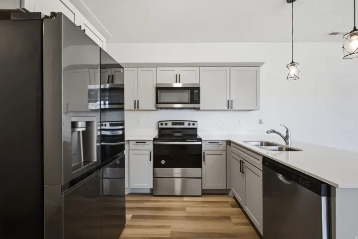 Modern kitchen featuring light gray cabinetry with dark hardware, white countertops, stainless steel appliances, and wood-finish flooring