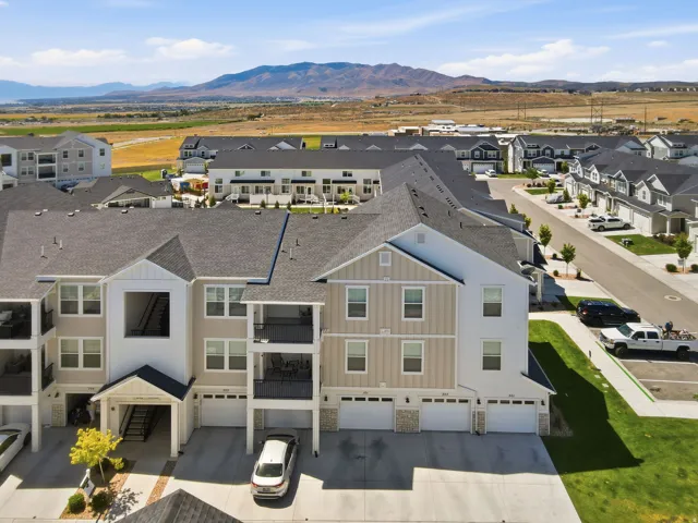 Multi-level residential building featuring private balconies with black railings, individual garages, and a light-toned exterior with stone accents
