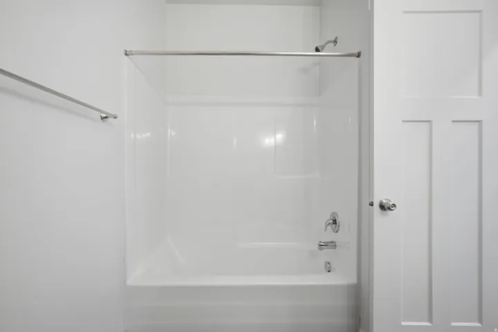 White tub and shower combination with chrome fixtures, a shower rod, and a towel bar