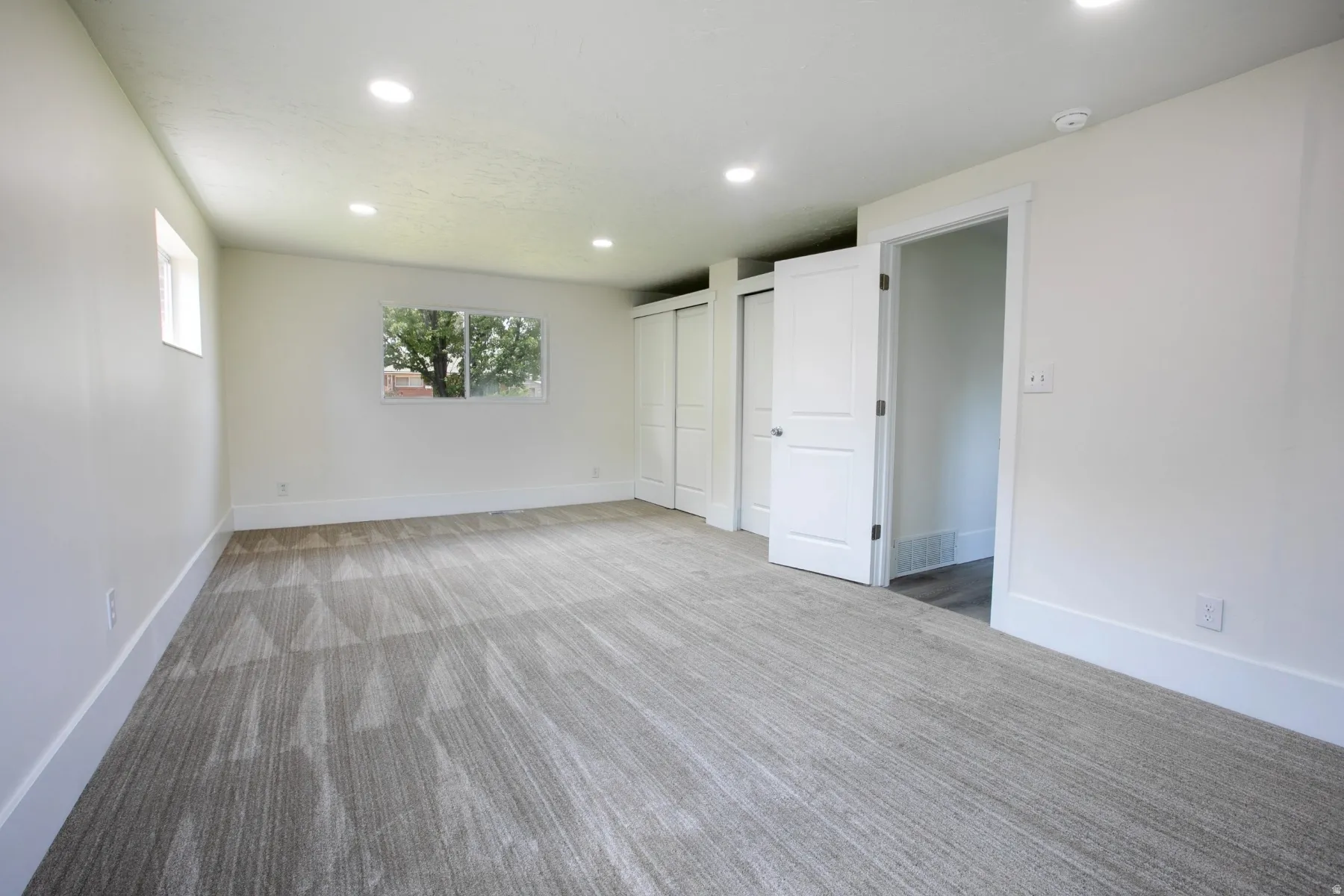Expansive room featuring a window, modern recessed lighting, white trim, and light-toned patterned carpet