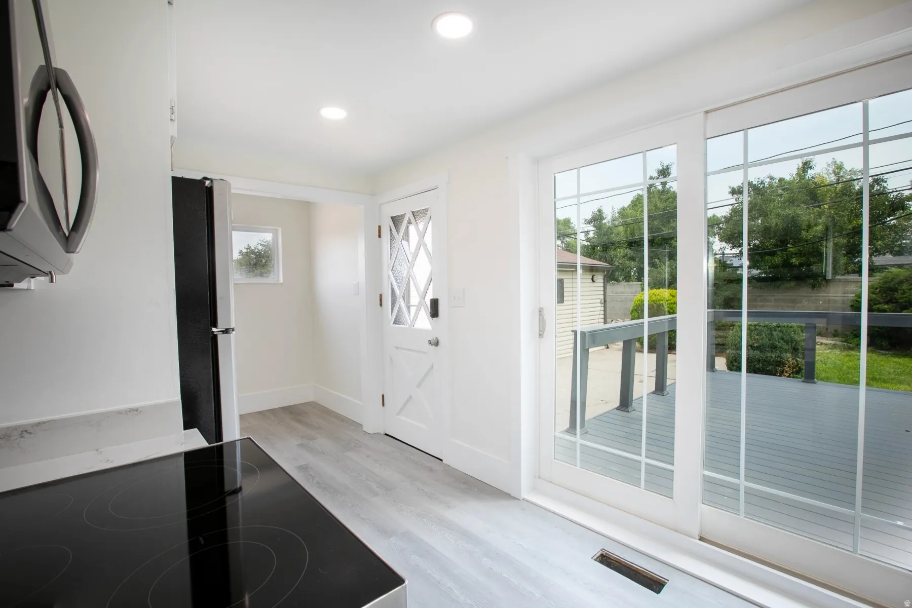 Light-filled interior featuring a black electric cooktop, light wood-finish flooring, and recessed ceiling lighting