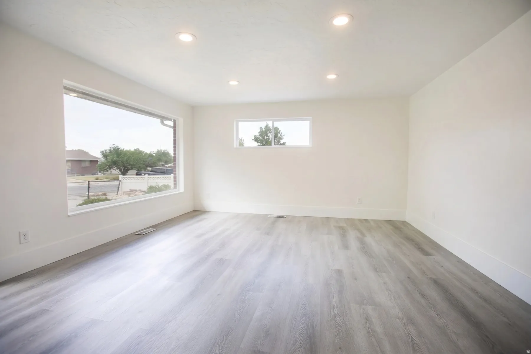 Spacious room featuring wood-finish flooring, white walls, recessed lighting, a large picture window, and a secondary window