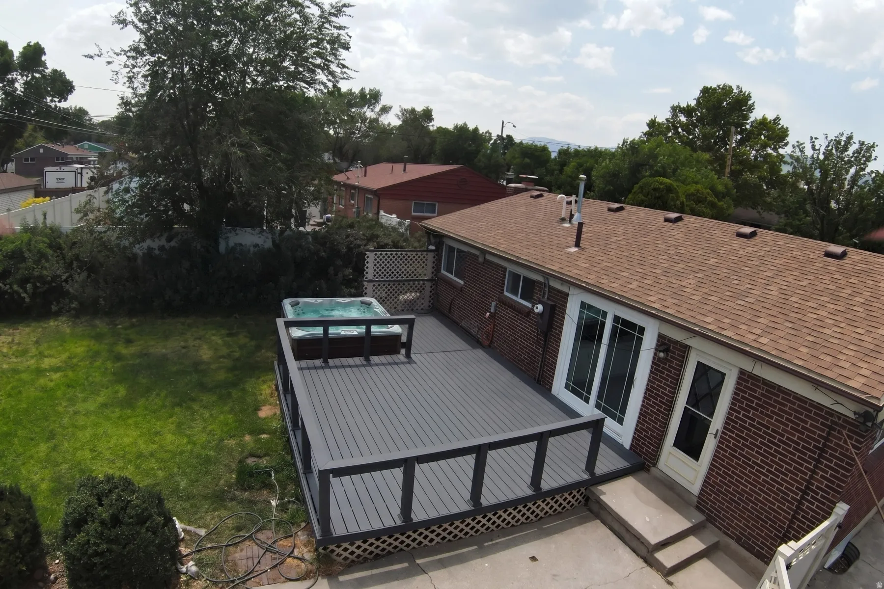 Spacious backyard with a large composite deck, integrated hot tub, and a manicured lawn