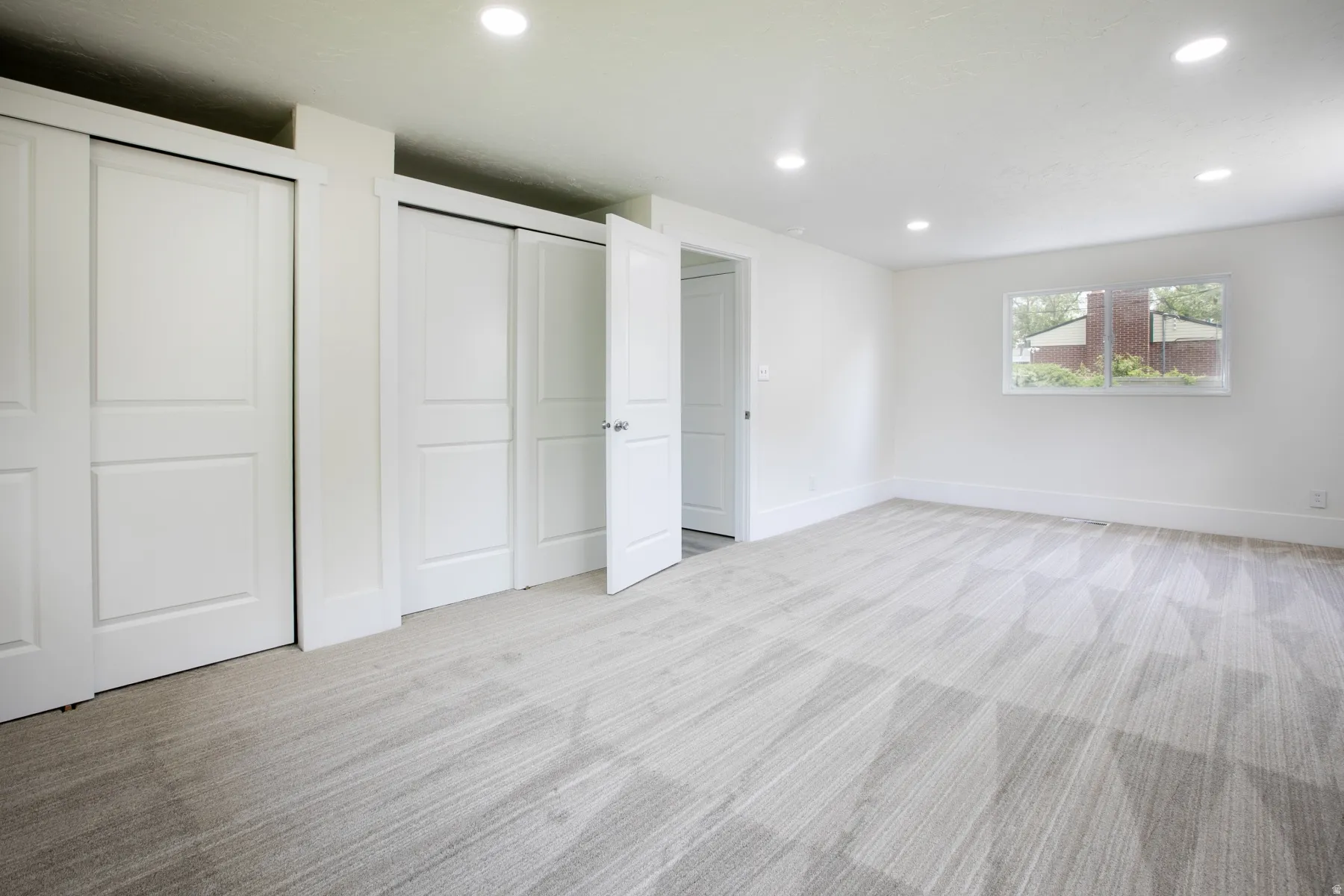 Bright interior space featuring a window with exterior shrubbery, recessed lighting, and a neutral-toned patterned carpet