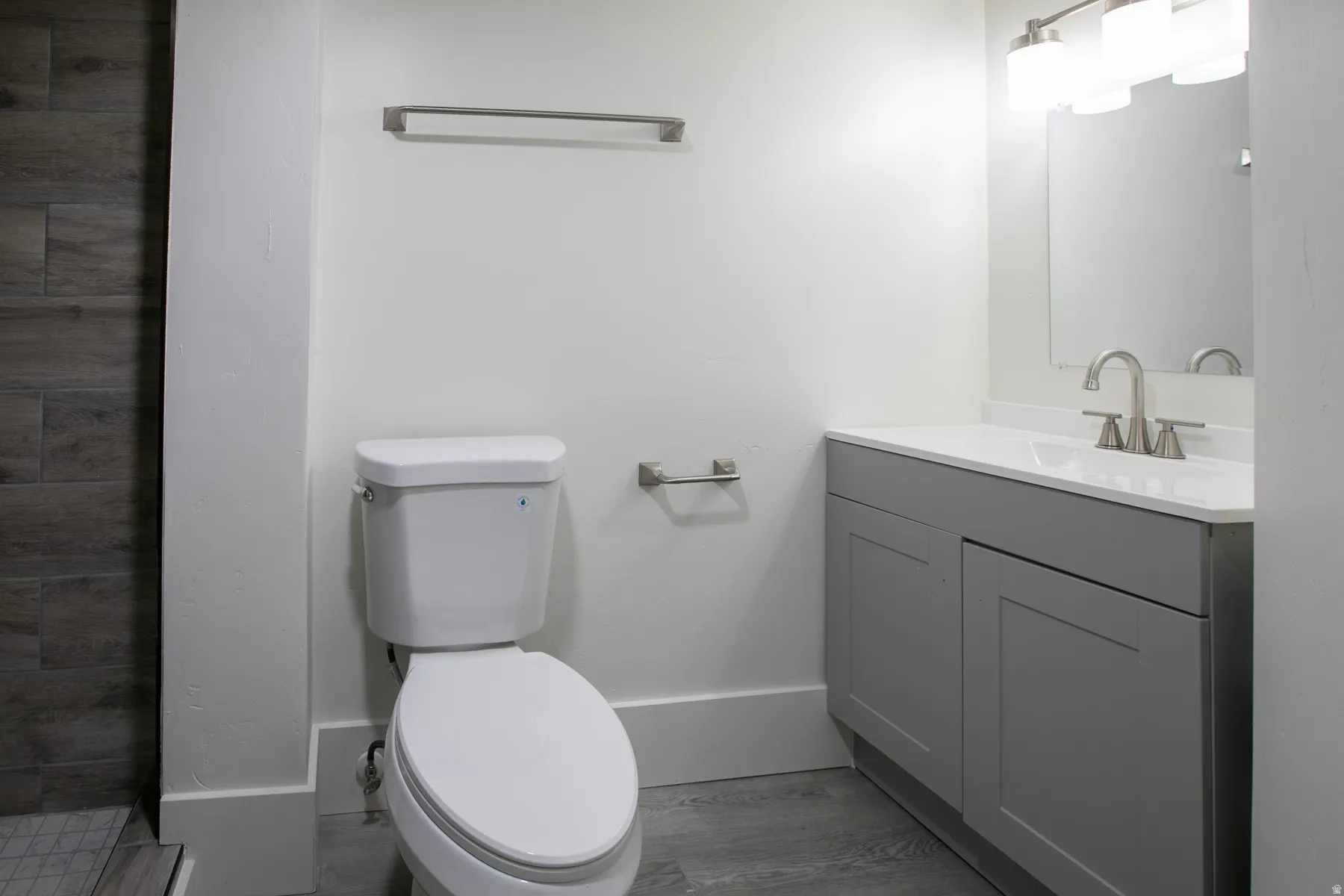 Bathroom featuring a white toilet, gray vanity with a white countertop and integrated sink, brushed nickel faucet, and wood-finish tile flooring