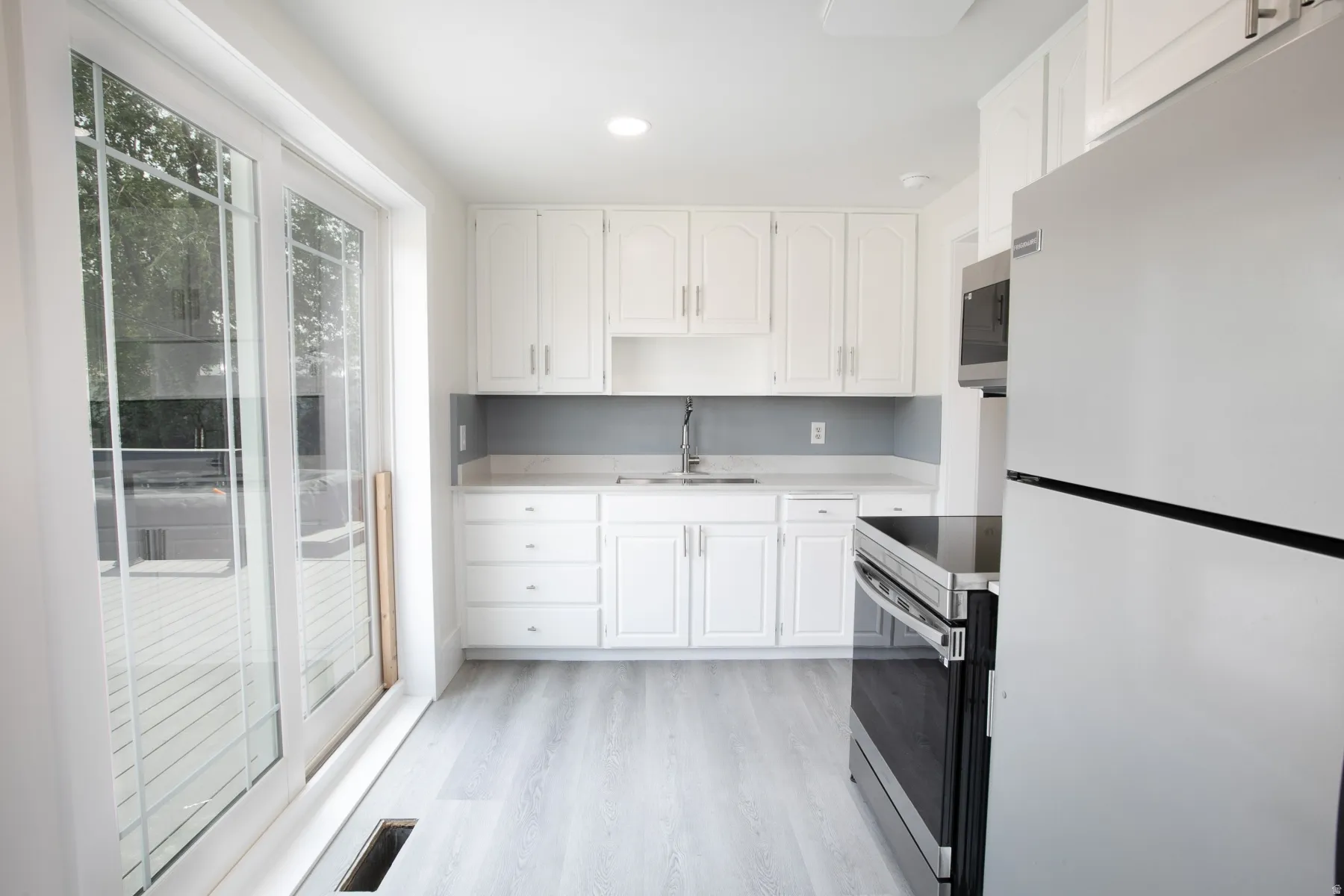 Bright kitchen featuring white cabinetry, light countertops, stainless steel appliances, wood-finish flooring, and sliding glass doors opening to an outdoor deck