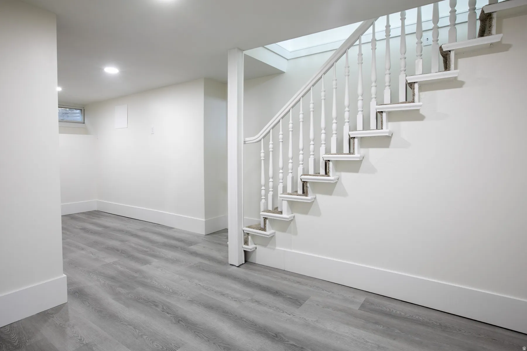 Finished lower level featuring a white painted staircase with turned balusters, recessed lighting, wood-finish flooring, and a casement window