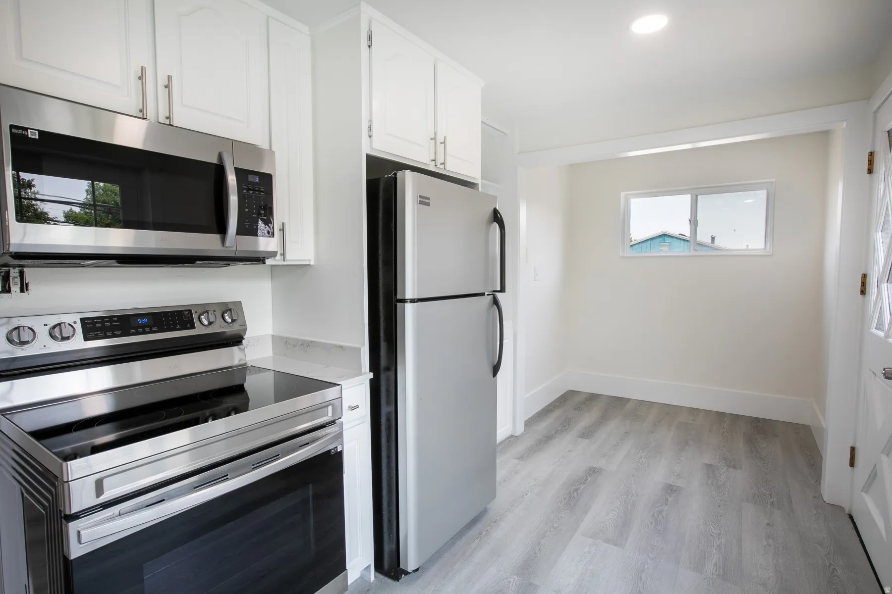 Kitchen featuring stainless steel appliances, white cabinetry, light-toned countertops, wood-finish flooring, and a recessed ceiling light