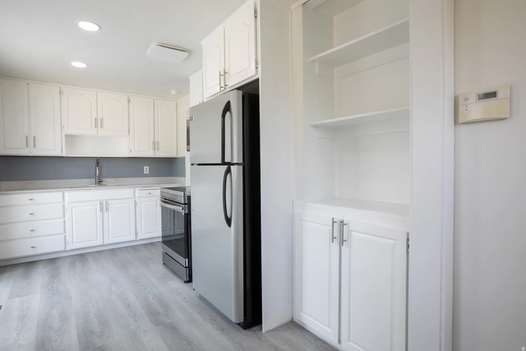 Bright kitchen featuring white cabinetry, stainless steel appliances, light gray countertops, and wood-finish flooring