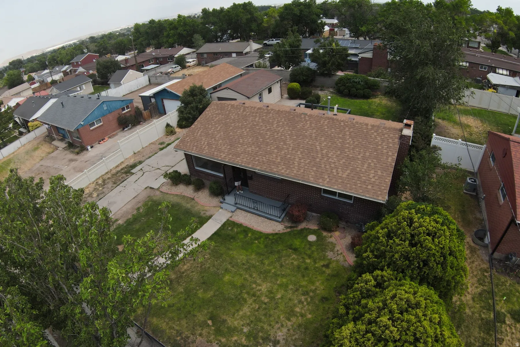 Brick residence featuring a brown shingle roof, front entry porch with railing, and a mature landscaped front yard