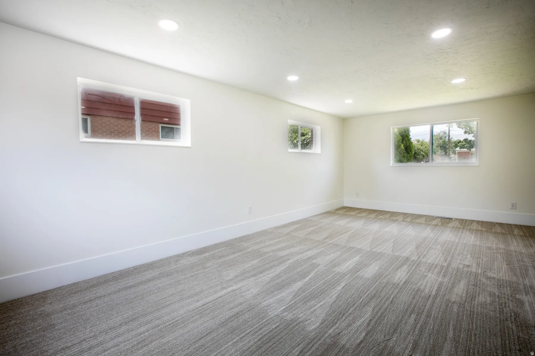Spacious room featuring new patterned carpeting, white baseboards, and neutral wall paint