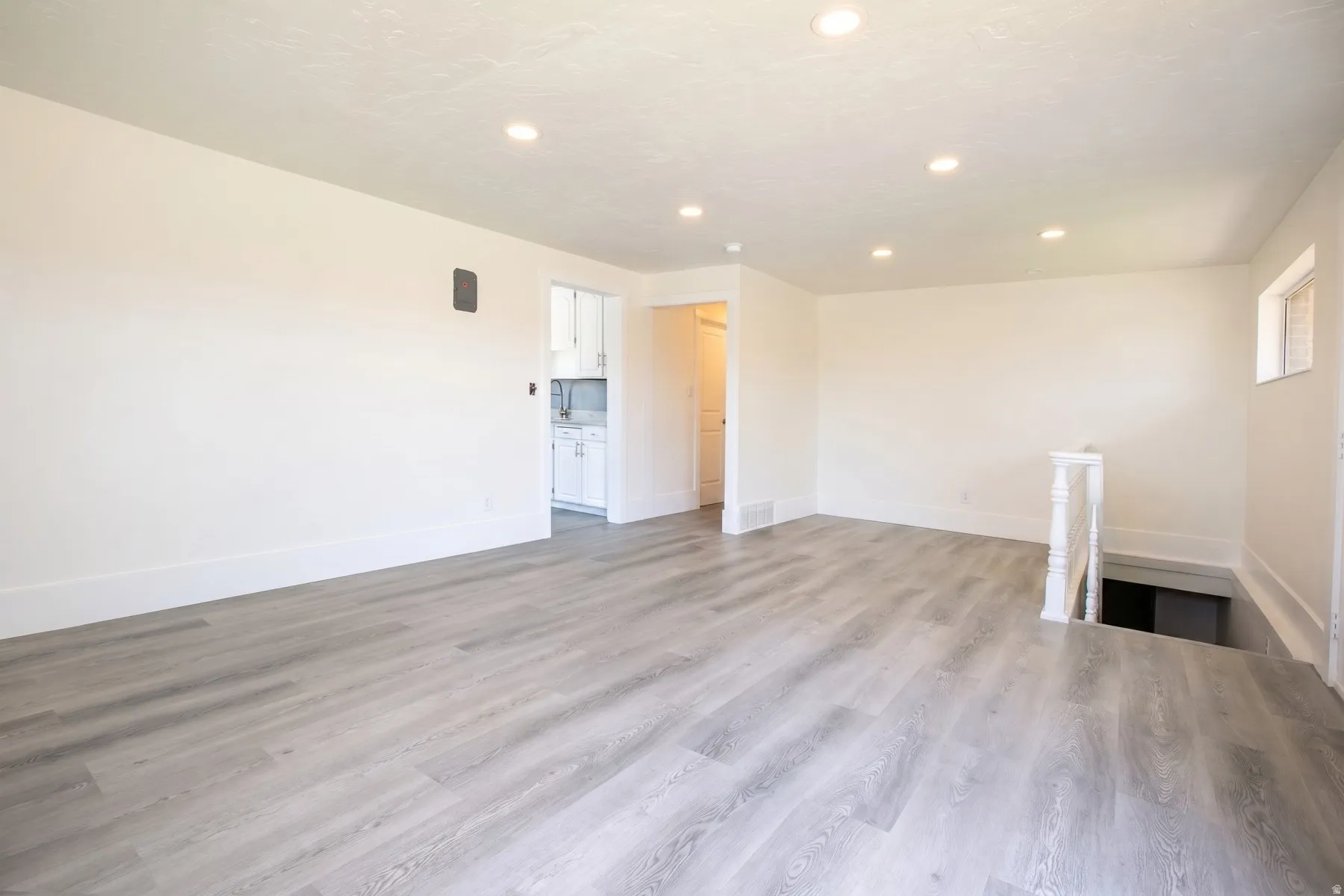 Spacious room featuring wood-finish flooring, recessed lighting, white walls, and white trim