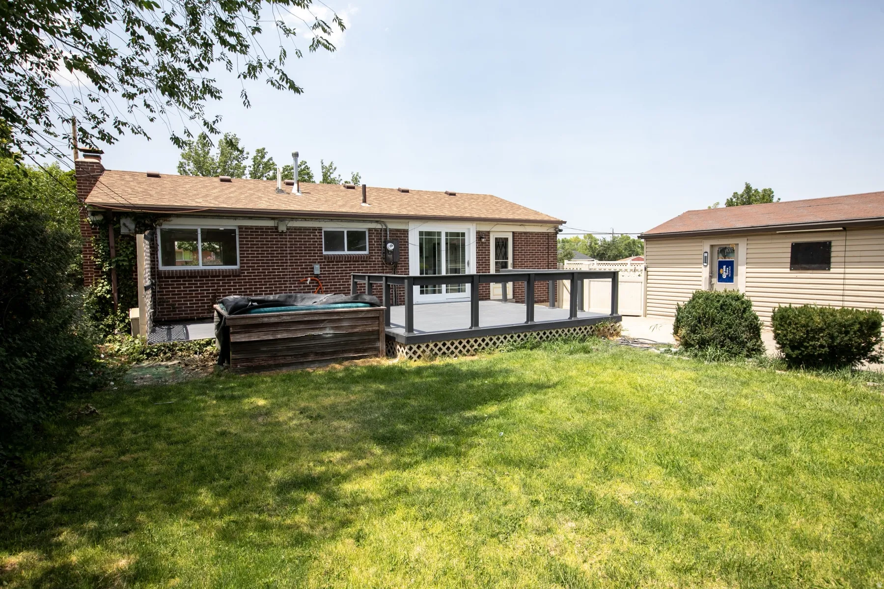 Expansive rear yard featuring a composite deck with dark railing, a built-in hot tub, and a separate outbuilding with siding