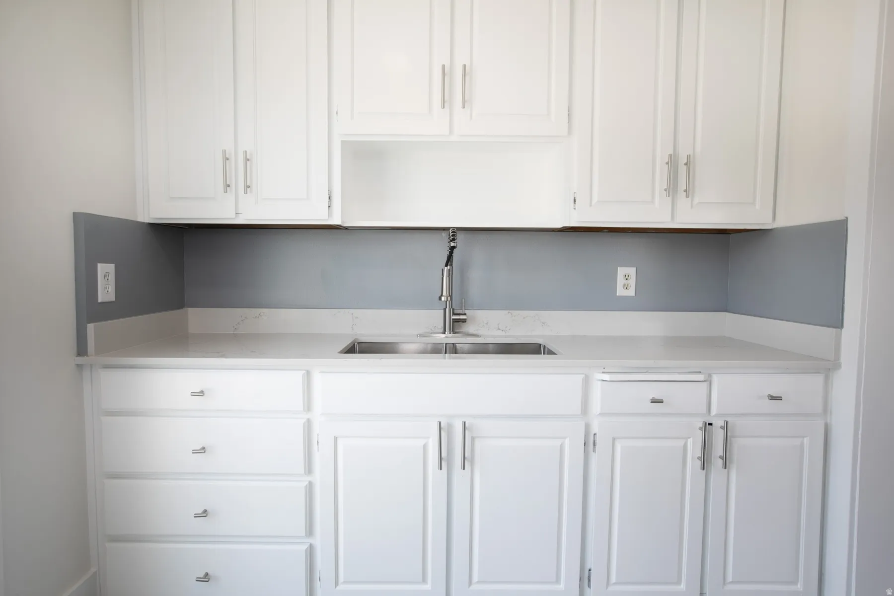 Kitchenette featuring white cabinetry, light countertops, a stainless steel double-basin sink, and a chrome faucet