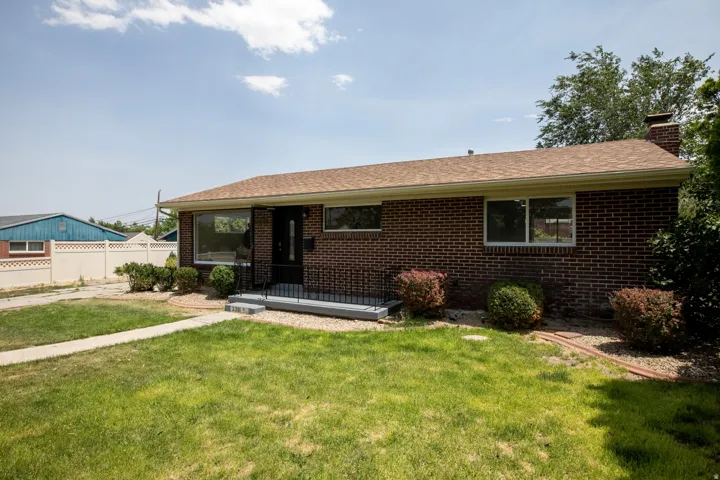 Brick exterior featuring a brown shingle roof, dark front door, and a concrete entry pad with black metal railings