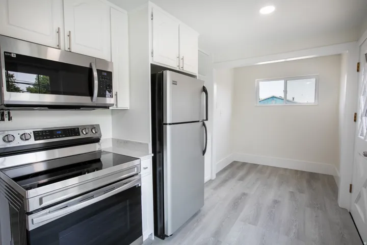 Kitchen featuring stainless steel appliances, white cabinetry, light-toned countertops, wood-finish flooring, and a recessed ceiling light