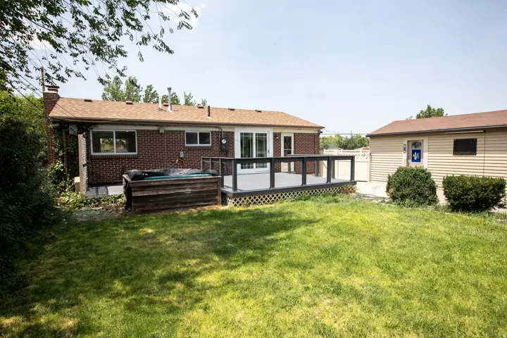 Expansive rear yard featuring a composite deck with dark railing, a built-in hot tub, and a separate outbuilding with siding