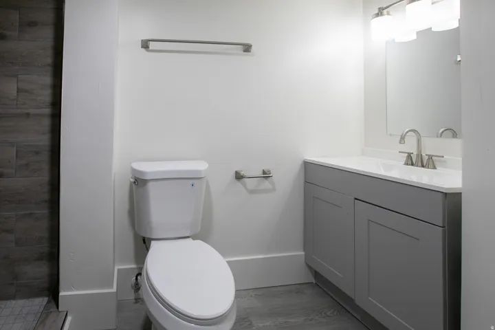 Bathroom featuring a white toilet, gray vanity with a white countertop and integrated sink, brushed nickel faucet, and wood-finish tile flooring
